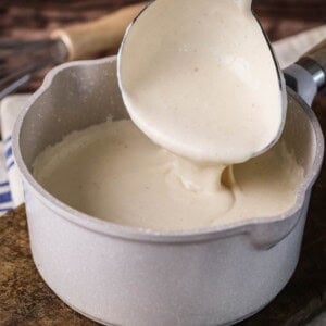 Béchamel in a saucepan with large ladle scooping some up showing how lusciously thick and creamy it is.