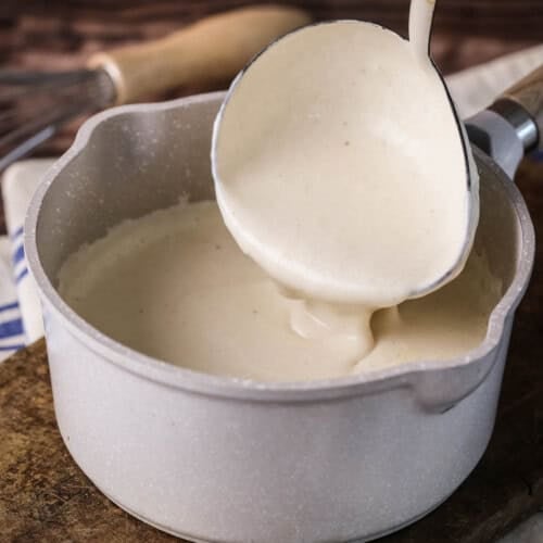 Béchamel in a saucepan with large ladle scooping some up showing how lusciously thick and creamy it is.
