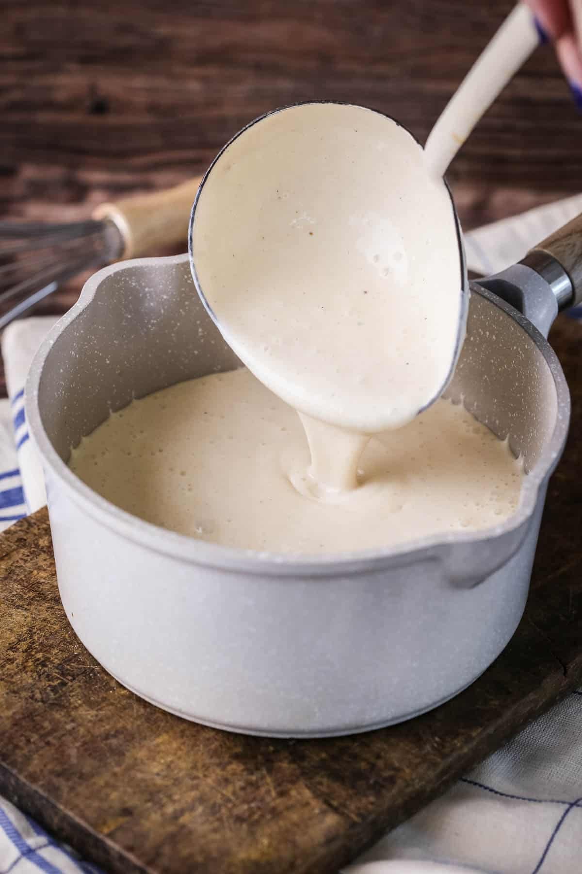 Béchamel in a saucepan with large ladle scooping some up showing how lusciously thick and creamy it is.
