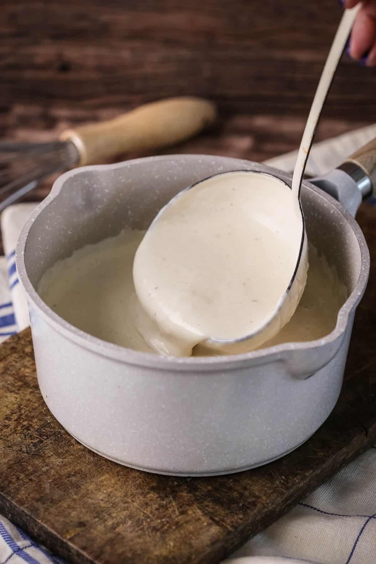 Béchamel in a saucepan with large ladle scooping some up showing how lusciously thick and creamy it is.
