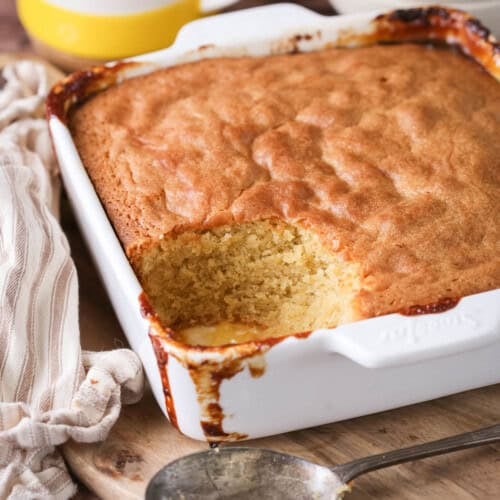 Lemon sponge pudding in a baking dish with a scoop taken out showing moist sponge.