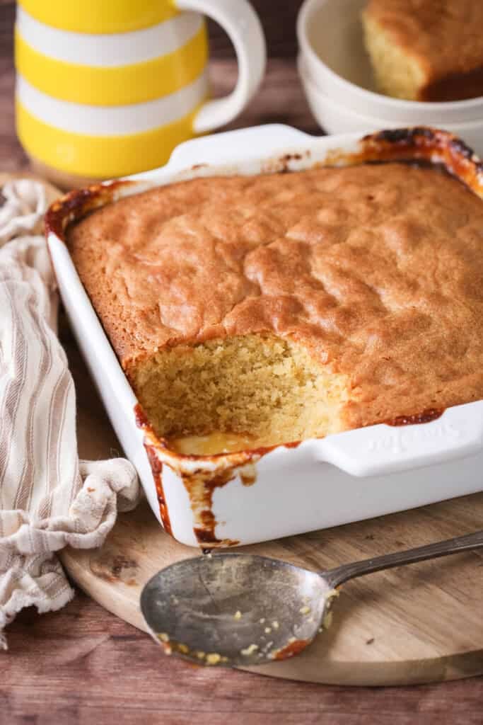 Lemon sponge pudding in a baking dish with a scoop taken out showing moist sponge.