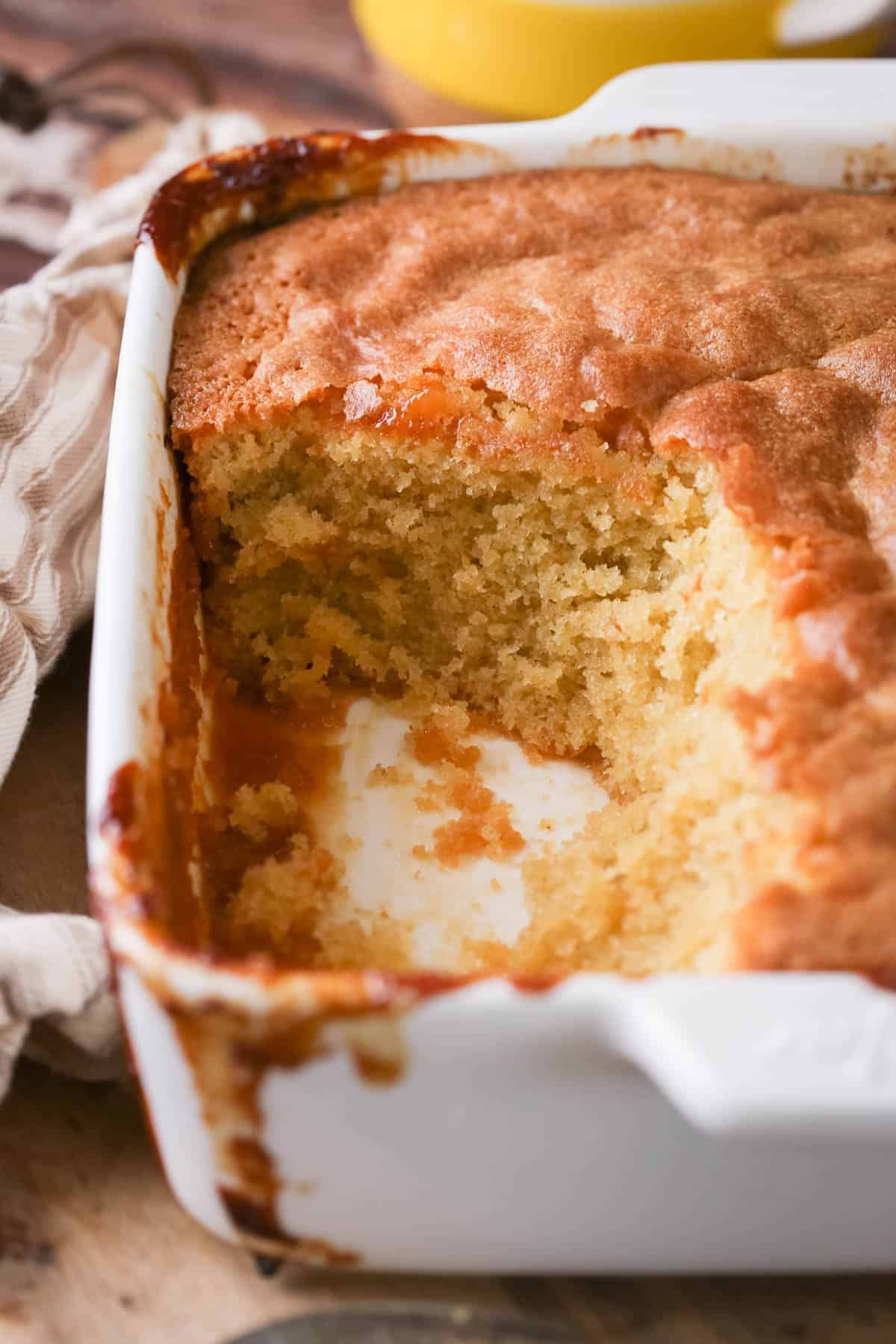 Lemon sponge pudding in a baking dish with a scoop taken out showing moist sponge.