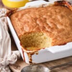 Lemon sponge pudding in a baking dish with a scoop taken out showing moist sponge.