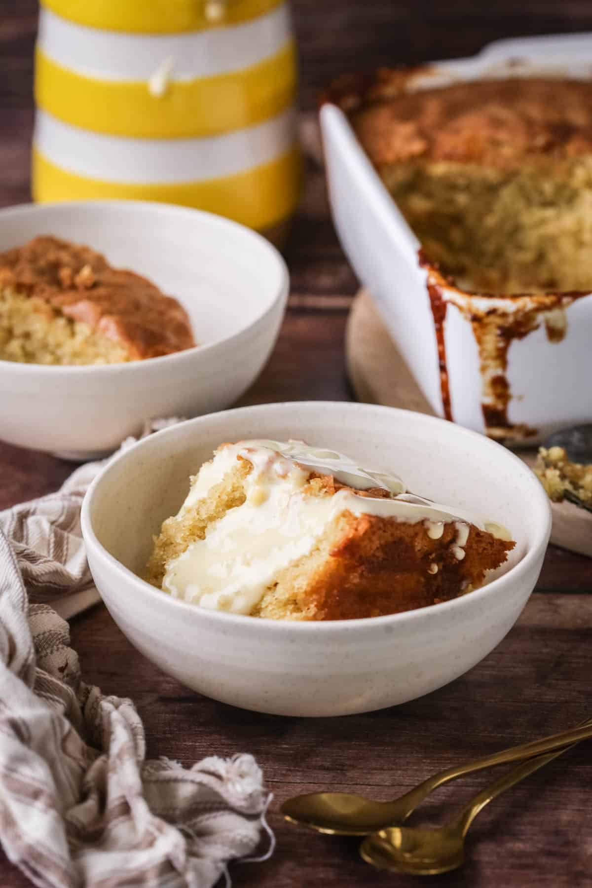 Portion of lemon pudding in a bowl with custard poured over top.