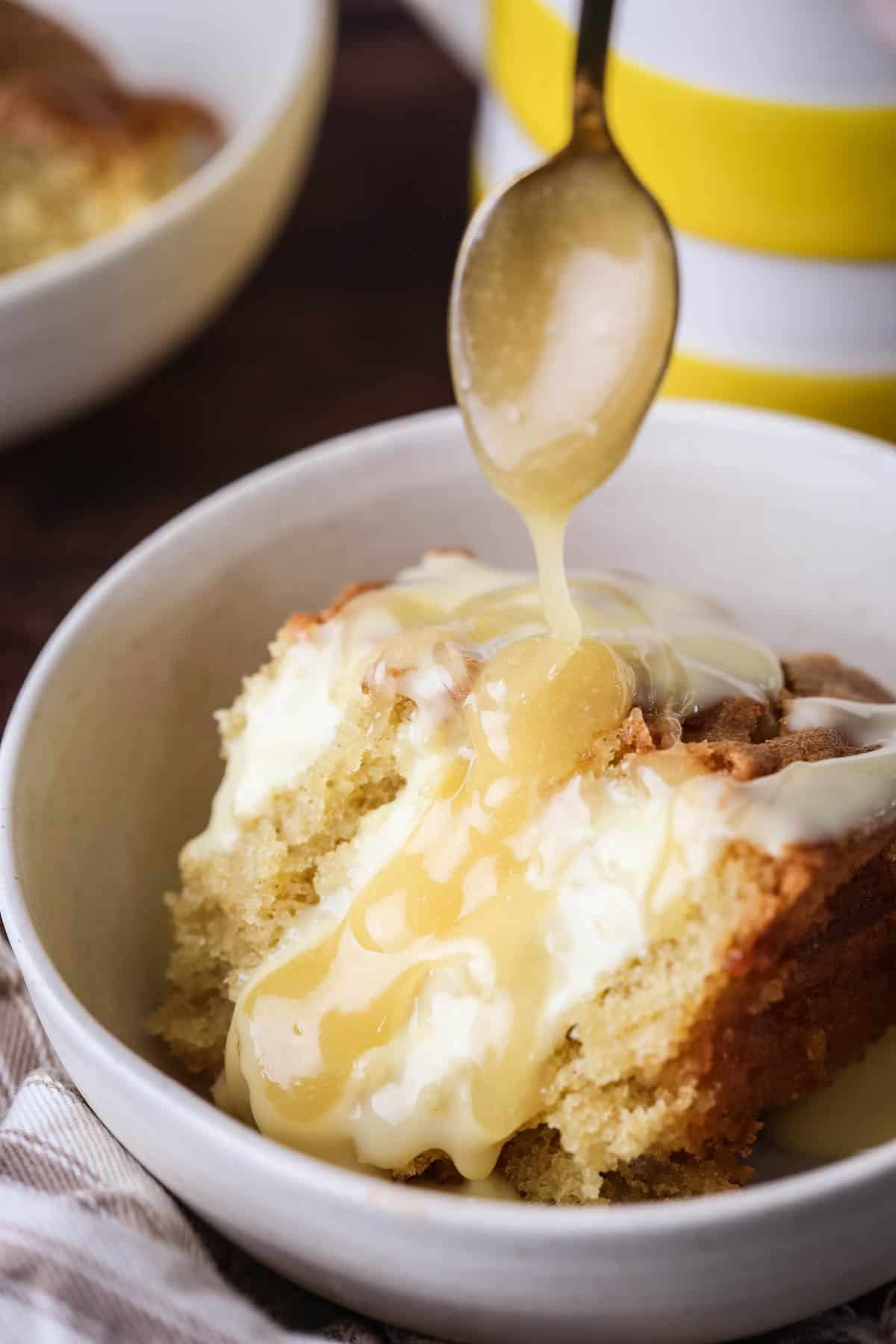 Portion of lemon pudding in a bowl with custard poured over top and extra lemon curd drizzled over.