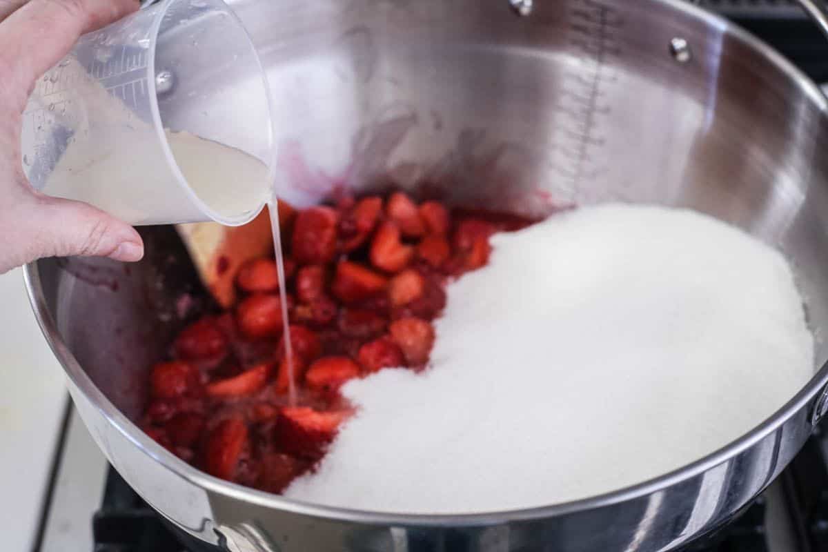 Lemon juice and sugar added to softened fruits in a maslin pan.