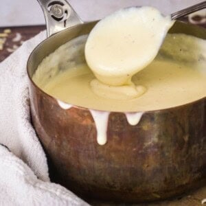 Spooning gluten-free cheese sauce from saucepan showing velvety creamy texture.