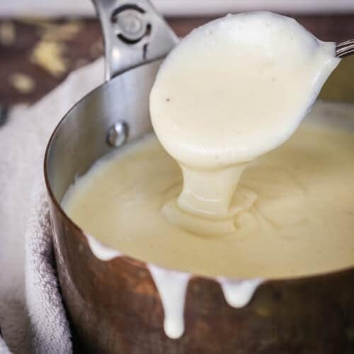Spooning gluten-free cheese sauce from saucepan showing velvety creamy texture.