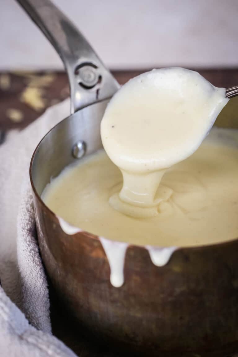 Spooning gluten-free cheese sauce from saucepan showing velvety creamy texture.
