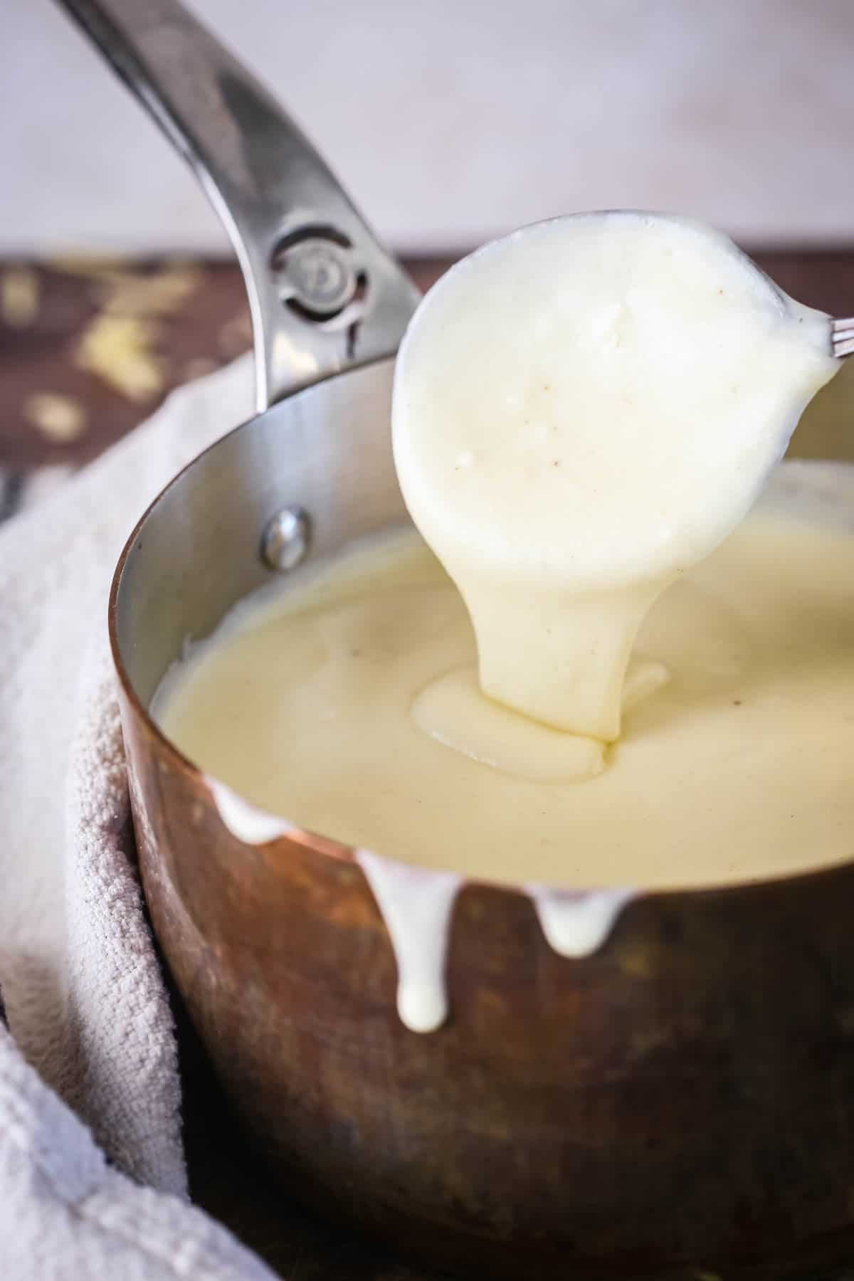Spooning gluten-free cheese sauce from saucepan showing velvety creamy texture.