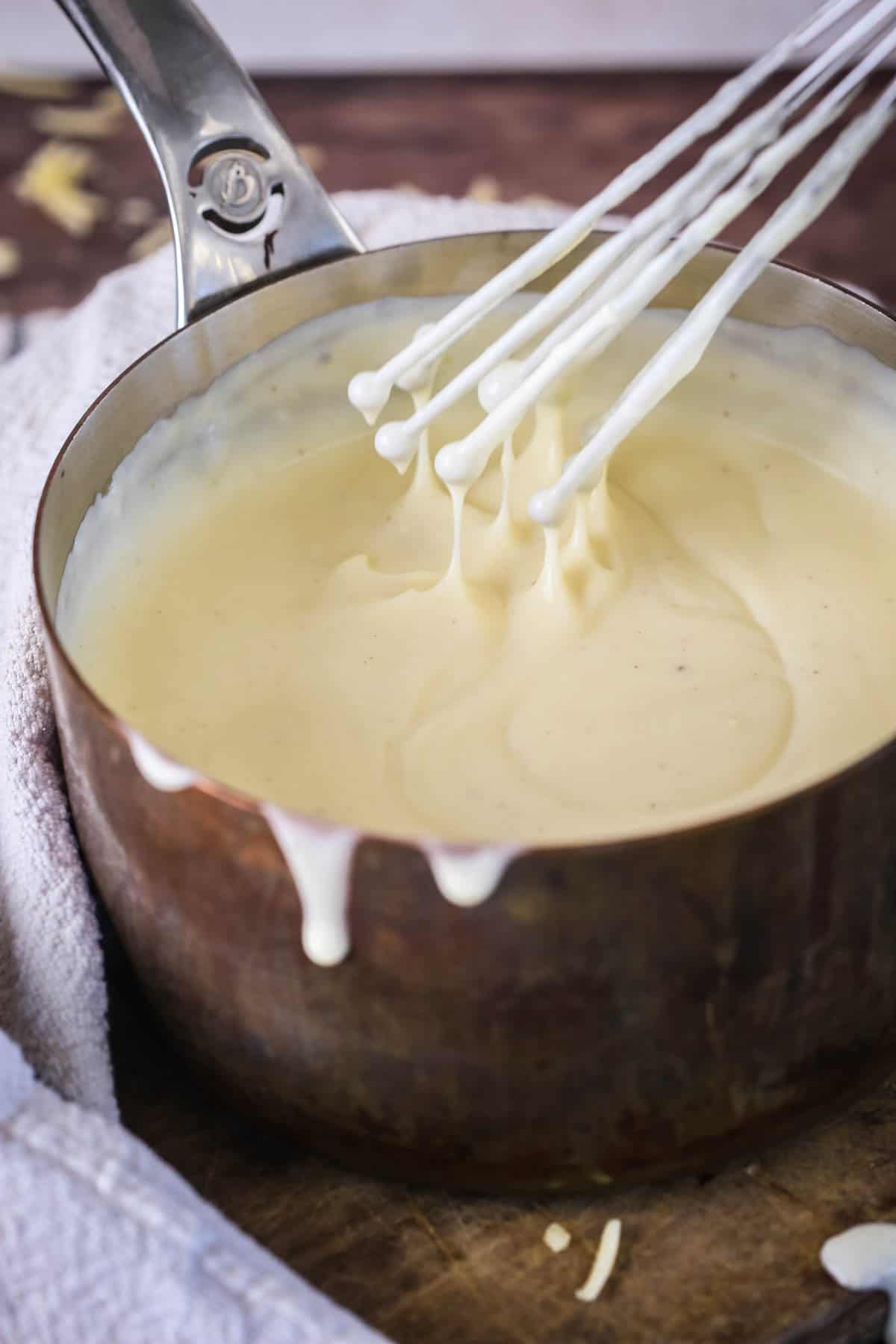 Spooning gluten-free cheese sauce from saucepan showing velvety creamy texture.
