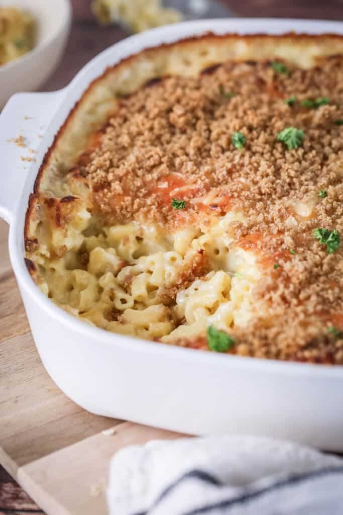 A portion of mac and cheese has been removed from serving dish showing ultra creamy and cheesy sauce clinging to tender macaroni pasta. With a golden crisp topping and fresh parsley.