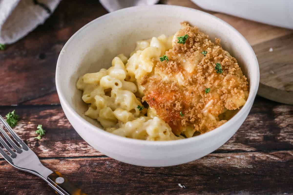 A portion of gluten-free mac and cheese in a bowl showing ultra creamy and cheesy sauce clinging to tender macaroni pasta. With a golden crisp topping.