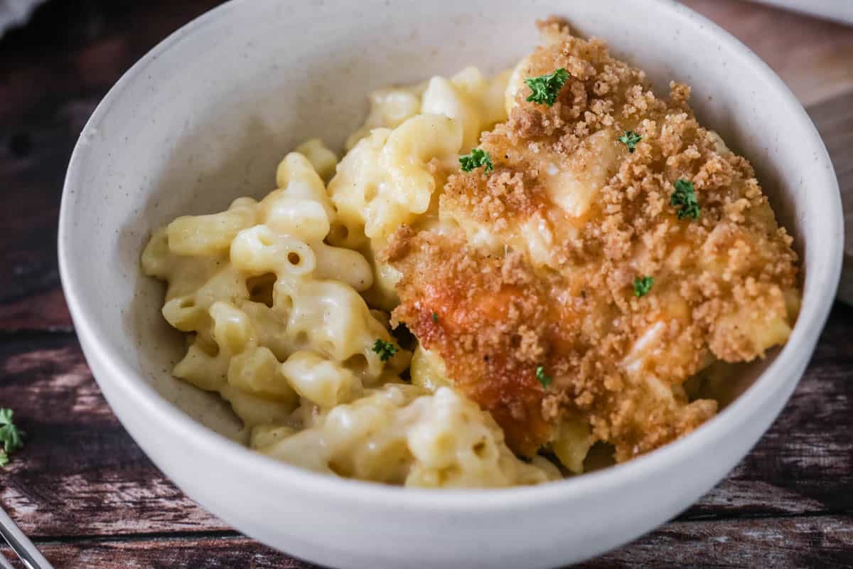 A portion of gluten-free mac and cheese in a bowl showing ultra creamy and cheesy sauce clinging to tender macaroni pasta. With a golden crisp topping.
