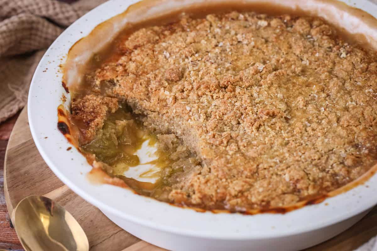 Gluten-Free Rhubarb Crumble in baking dish. with a portion removed showing thick and jammy rhubarb filling.