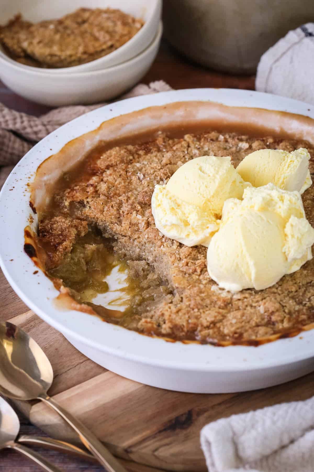 Gluten-Free Rhubarb Crumble in baking dish. with a portion removed showing thick and jammy rhubarb filling. With ice cream on top.