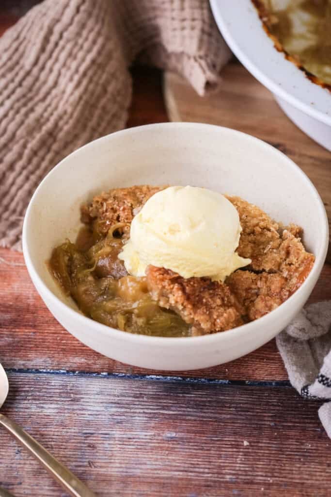 Gluten-Free Rhubarb Crumble served into a bowl with ice cream melting on top.