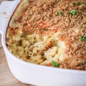 A portion of mac and cheese has been removed from serving dish showing ultra creamy and cheesy sauce clinging to tender macaroni pasta. With a golden crisp topping and fresh parsley.