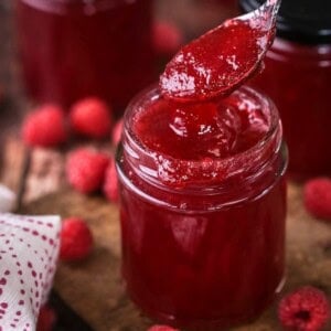 Teaspoon spooning out raspberry jam from pot showing thick but soft jam set with no seeds.