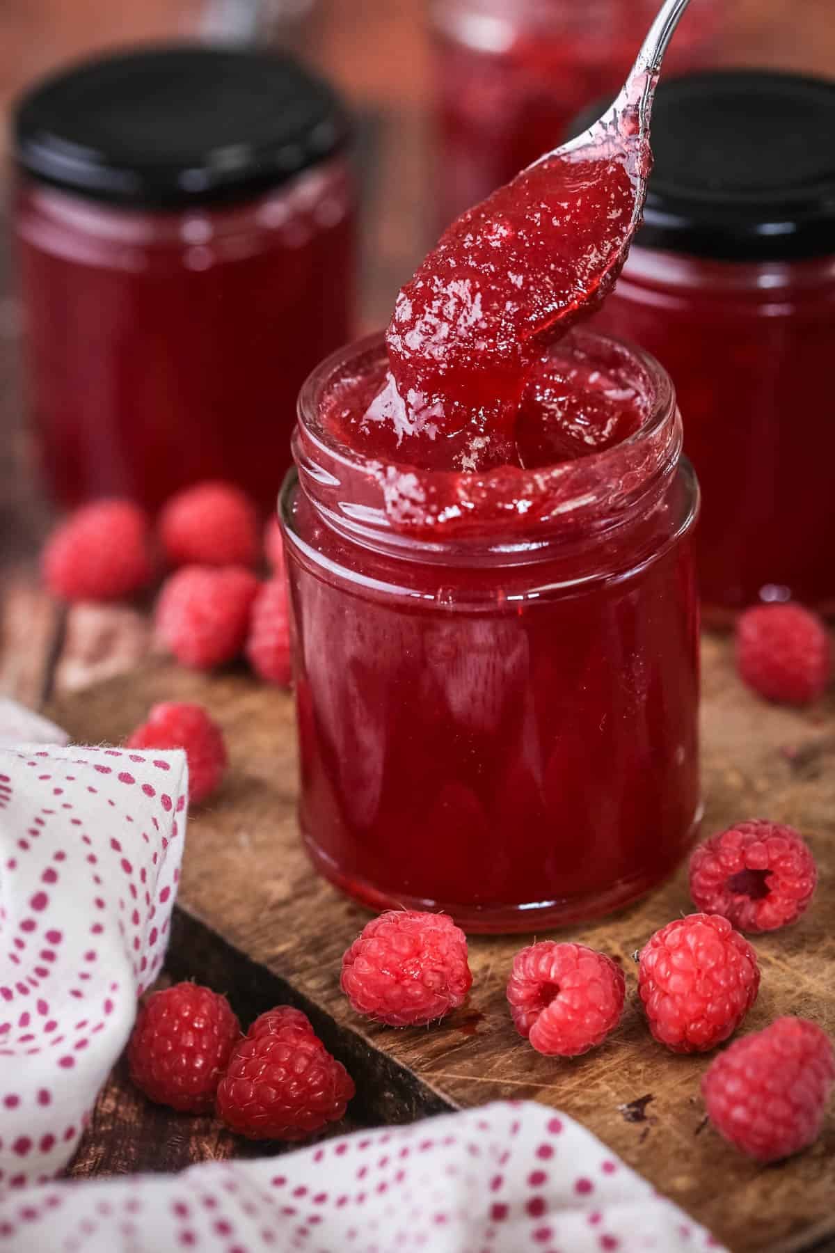 Teaspoon spooning out raspberry jam from pot showing thick but soft jam set with no seeds.