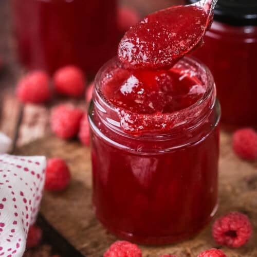 Teaspoon spooning out raspberry jam from pot showing thick but soft jam set with no seeds.