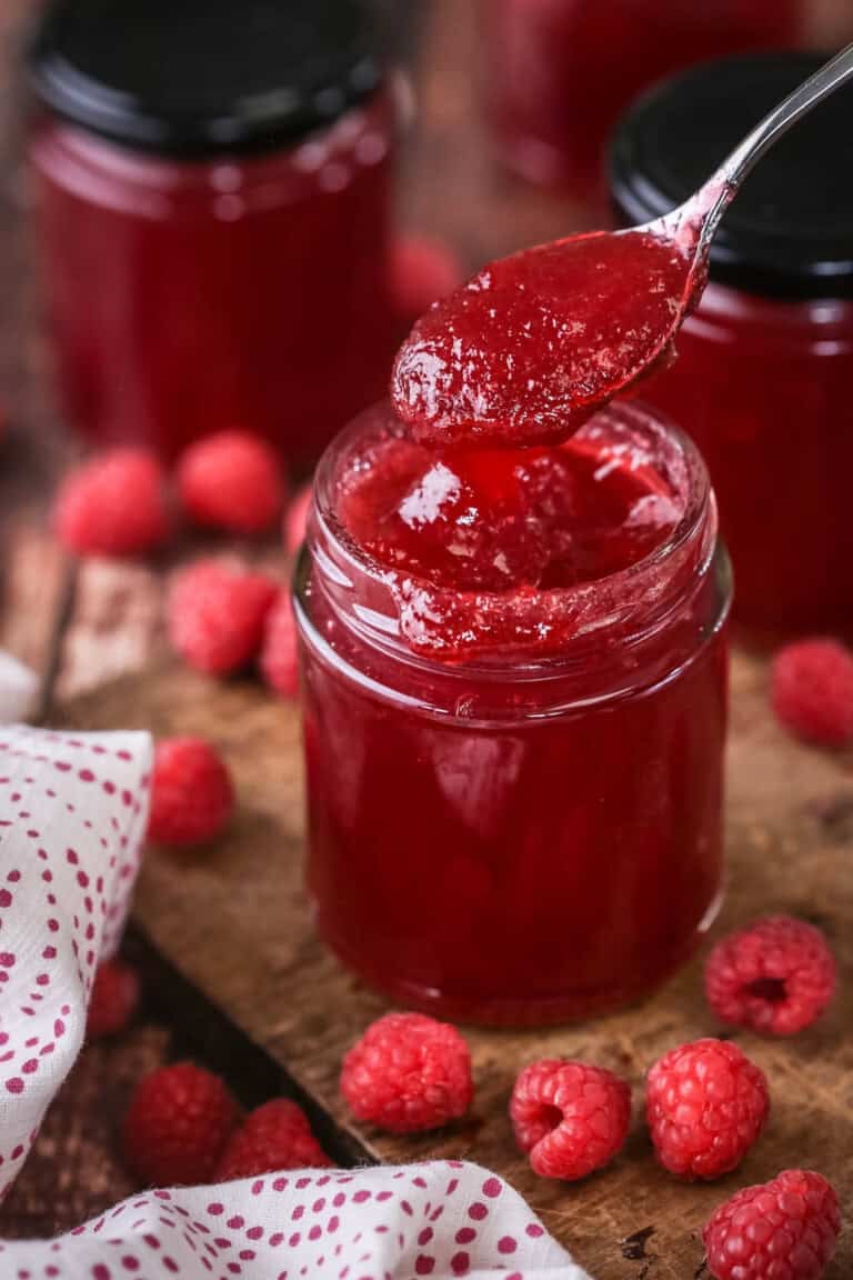 Teaspoon spooning out raspberry jam from pot showing thick but soft jam set with no seeds.