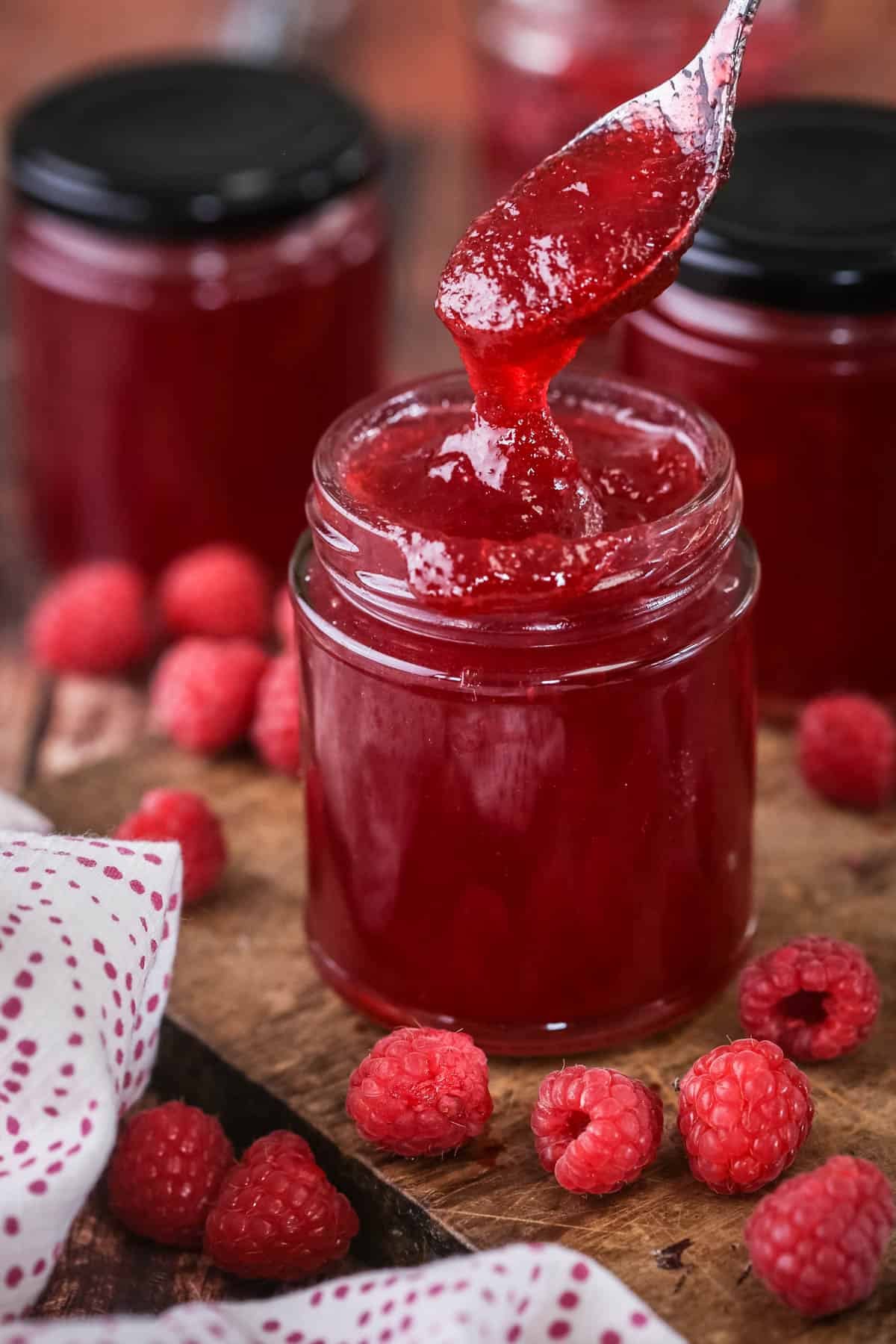 Teaspoon spooning out raspberry jam from pot showing thick but soft jam set with no seeds.