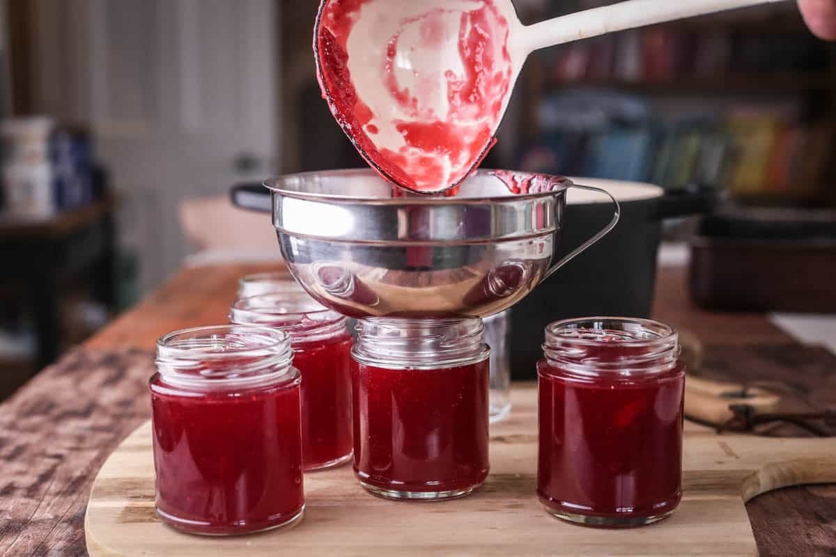 Ladle pouring jam into pots using jam funnel.