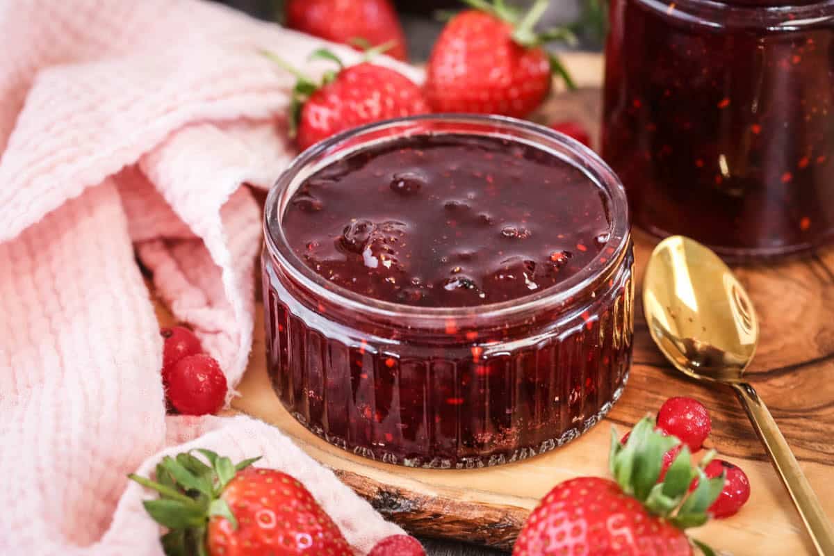 Pot of strawberry redcurrant jam surrounded by berries.