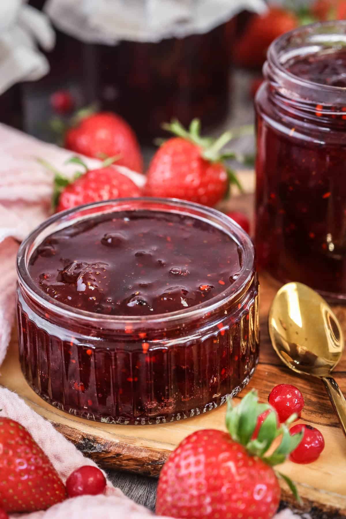 Pot of strawberry redcurrant jam surrounded by berries.