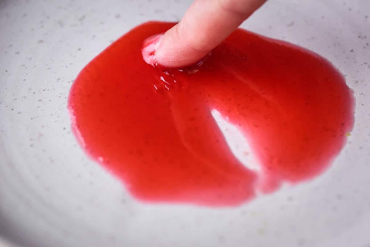 Finger pushing into jam on a saucer and there is no wrinkle and the jam is pooling back together. This shows the jam is underset.