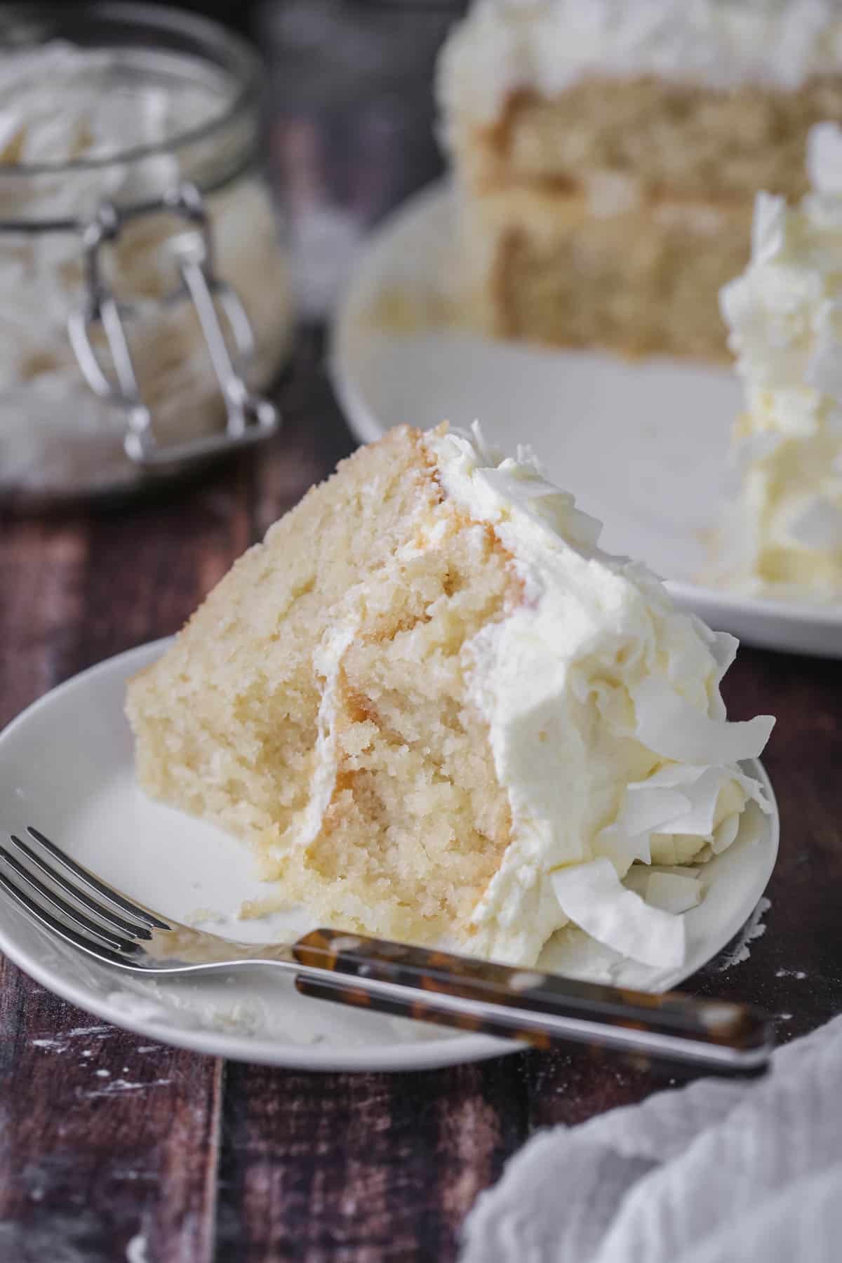 Soft, moist and fluffy slice of gluten-free Coconut Cake on a plate with forkfuls taken out showing the tender crumb.