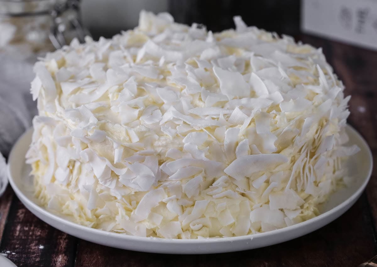 Gluten-Free Coconut Cake covered in coconut flakes on a white plate.