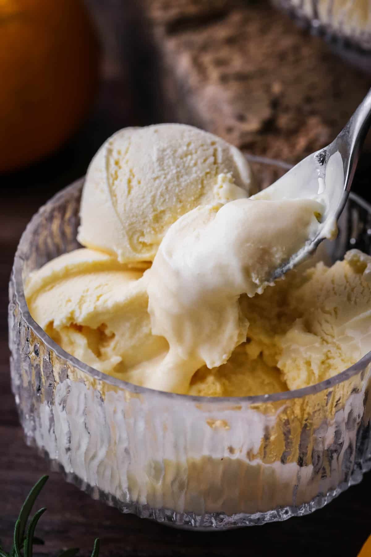 Orange ice cream in a glass bowl, spooning out ultra creamy mixture.