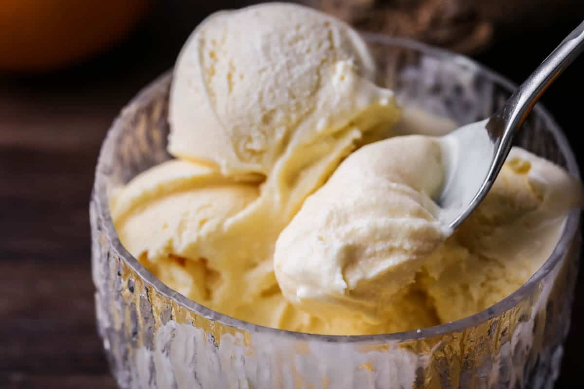 Orange ice cream in a glass bowl, spooning out ultra creamy mixture.