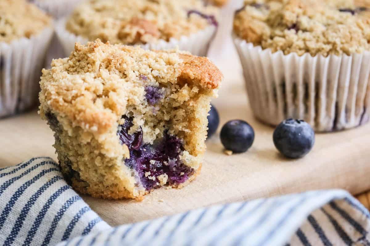 Blueberry Muffin on a table with a bite taken out showing juicy blueberries and soft fluffy crumb.