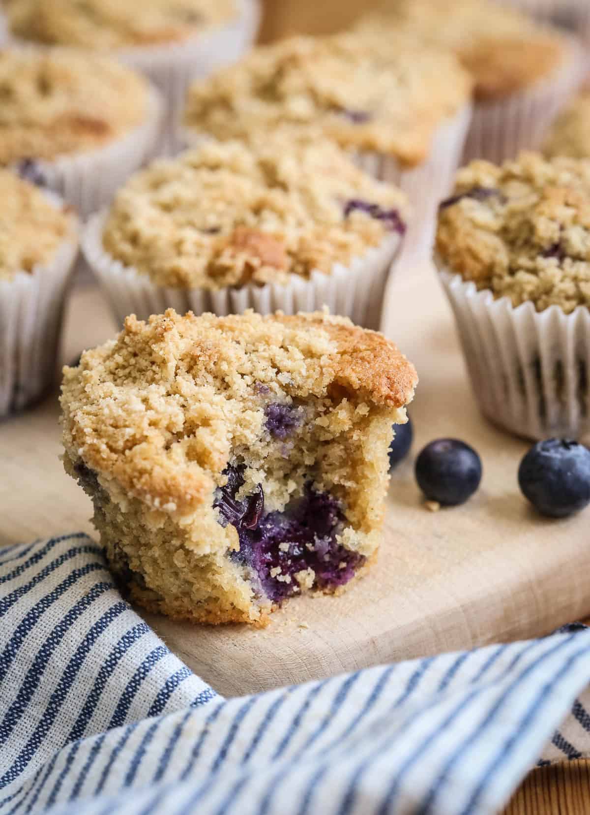 Blueberry Muffin on a table with a bite taken out showing juicy blueberries and soft fluffy crumb.