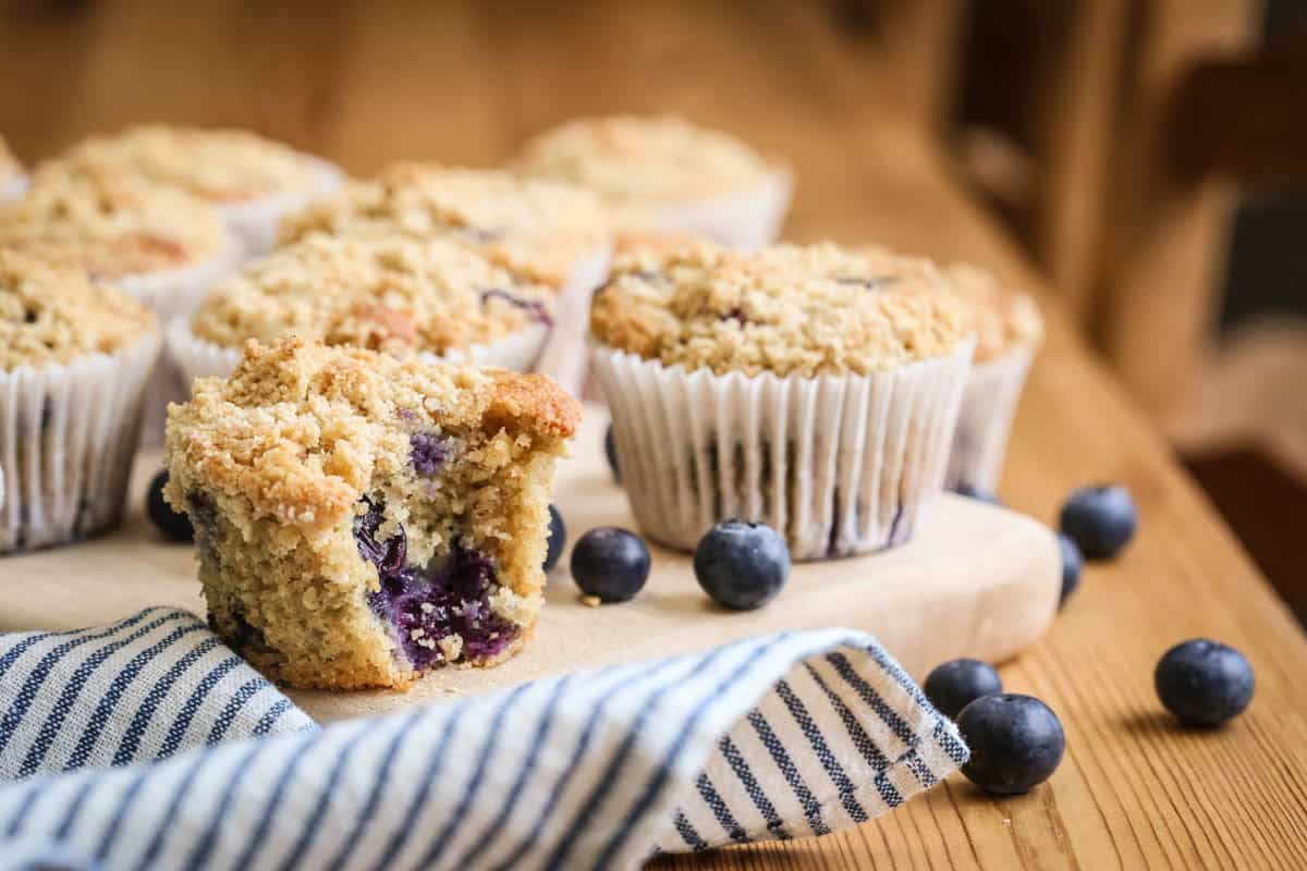 Blueberry Muffin on a table with a bite taken out showing juicy blueberries and soft fluffy crumb.