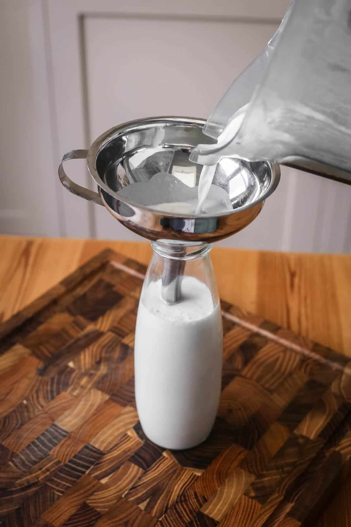 Cashew milk poured out of blender into milk bottle to store.