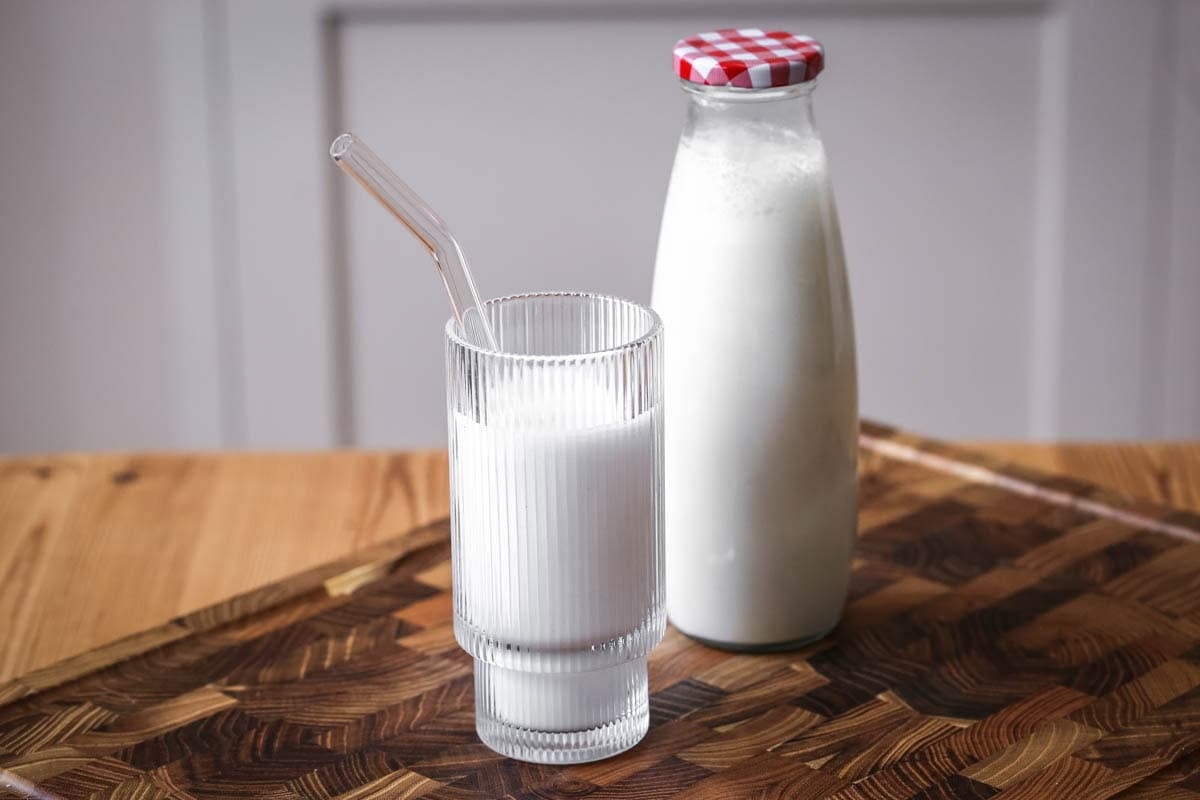 Cashew Nut Milk in a glass in front of full milk bottle, showing frothy creamy milk.