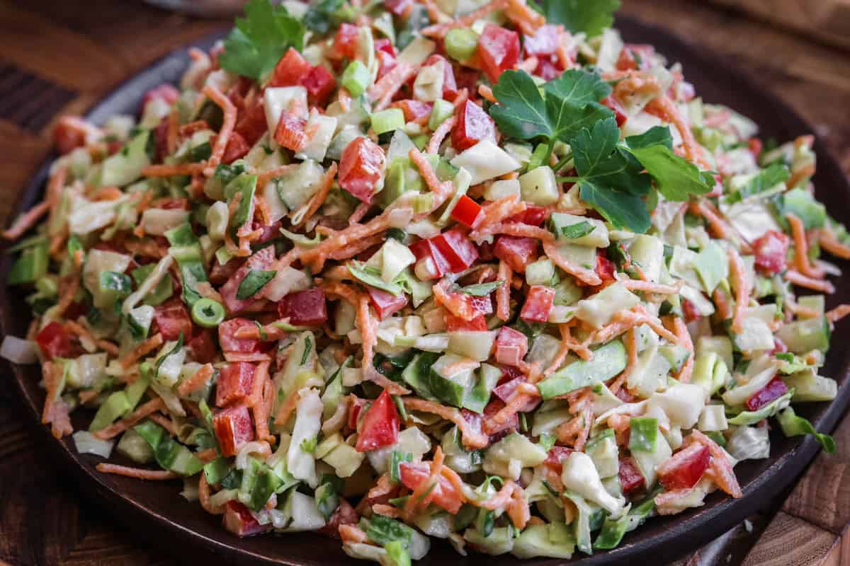 Crunchy Chopped Salad fully dressed and topped with fresh parsley leaves on a serving plate.