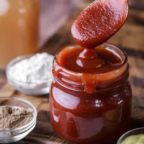 Spoon dipping out of a jar of BBQ sauce showing how it's thick and luscious.