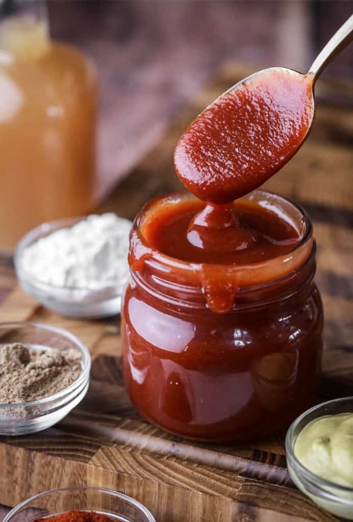 Spoon dipping out of a jar of BBQ sauce showing how it's thick and luscious.