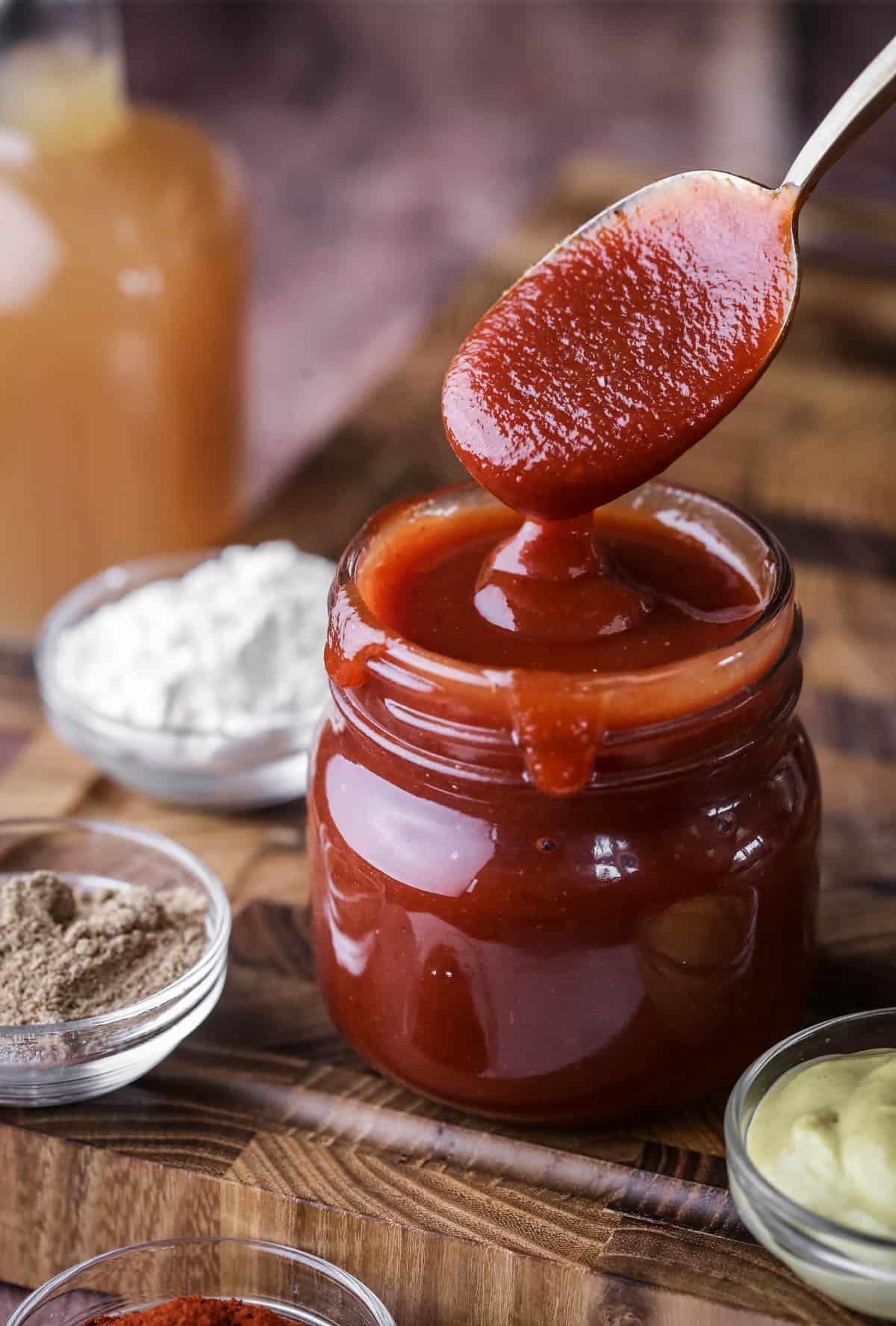 Spoon dipping out of a jar of BBQ sauce showing how it's thick and luscious.