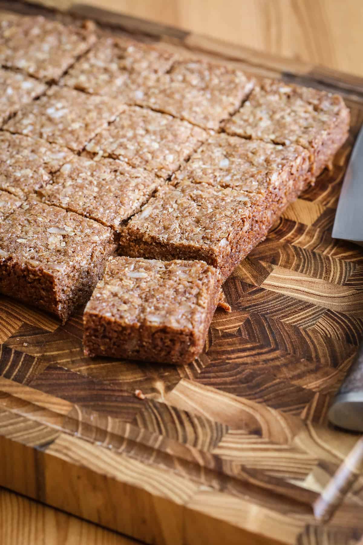 Flapjacks cut into perfect squares on wooden board with chef's knife.