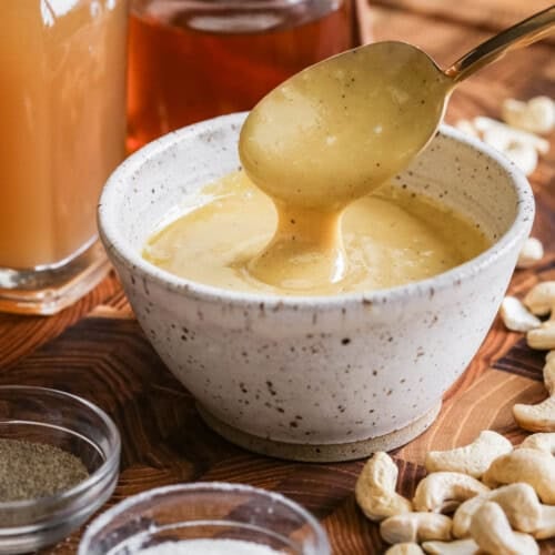 Spoon lifting out ultra creamy cashew dressing from a bowl.