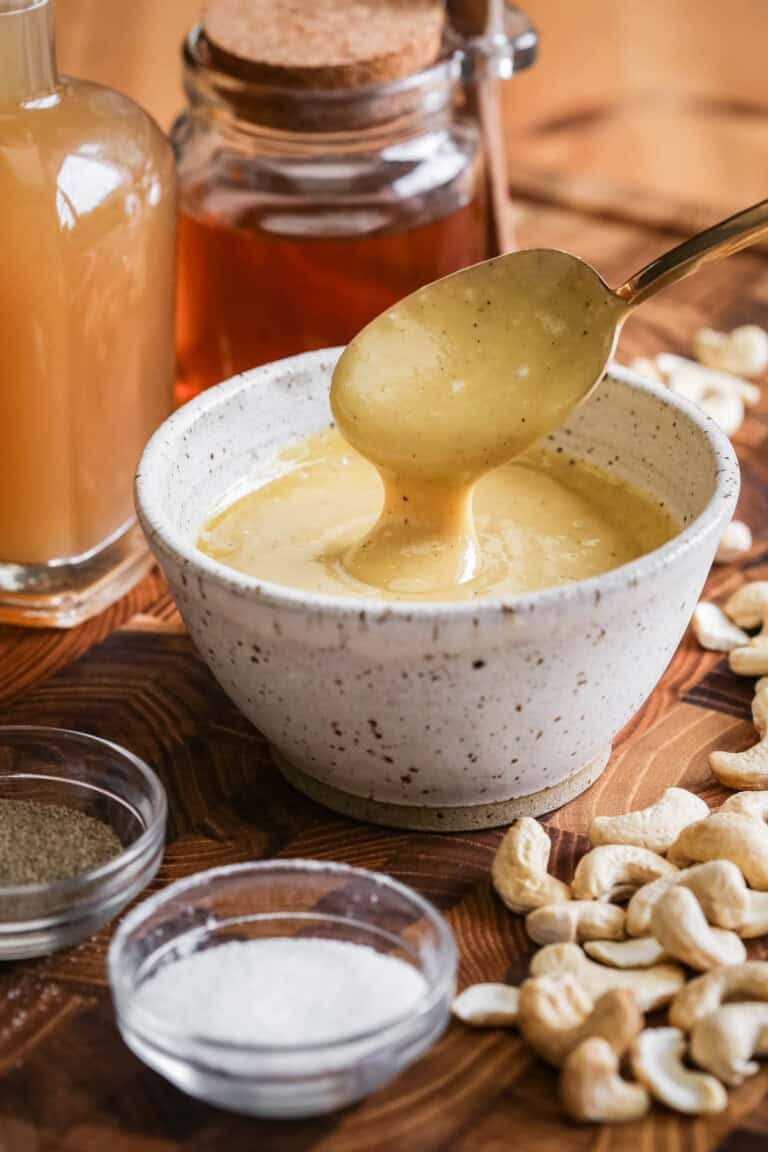 Spoon lifting out ultra creamy cashew dressing from a bowl.