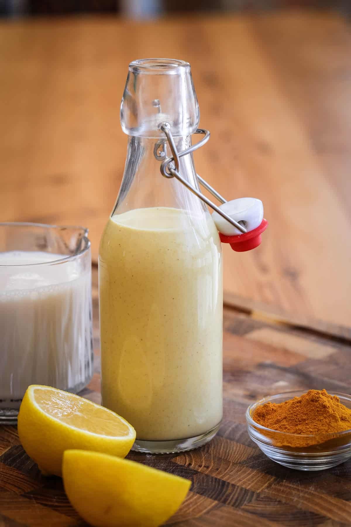 Tahini dressing in a clip top bottle surrounded by plant milk, lemon and turmeric.
