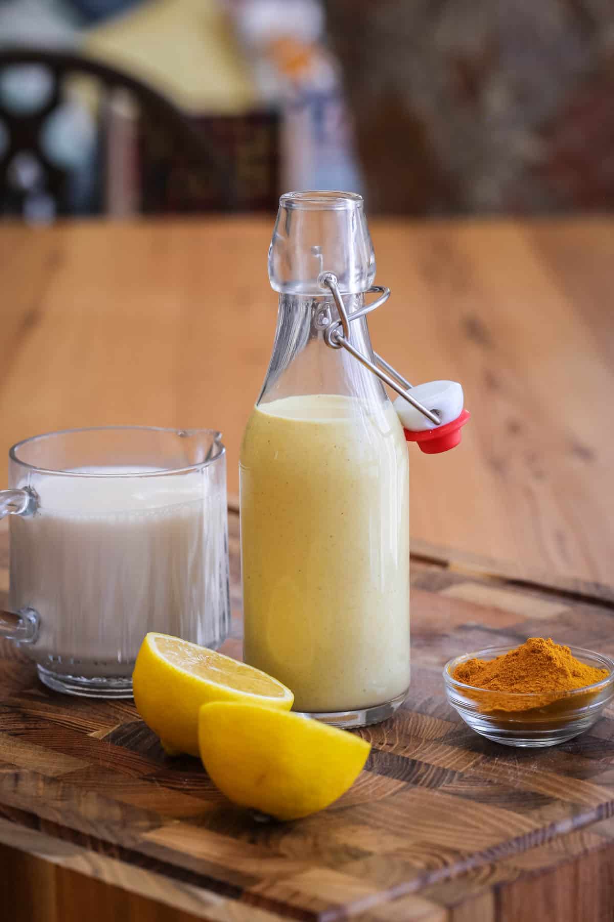 Tahini dressing in a clip top bottle surrounded by plant milk, lemon and turmeric.